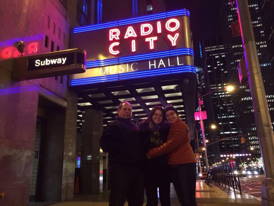 People posing under the Radio City Music Hall sign in NYC.